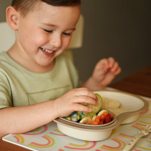 Toddler boy picks vegetables from littles sectioned bowl nested in dinner plate for children.